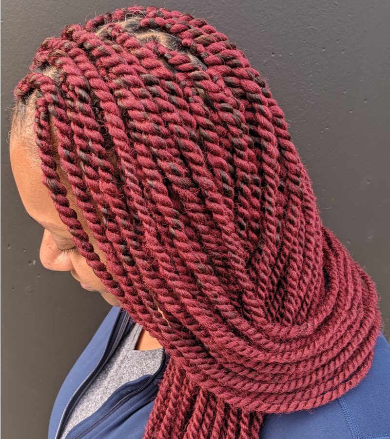 Jonge Afro-Amerikaanse vrouw met kinky twists en rood gevlochten haar zit in zakelijke professionele kleding