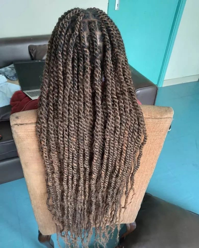 Vrouw met lange kinky twists laat ze vloeien over een bruine stoel terwijl ze in een woonkamer zit