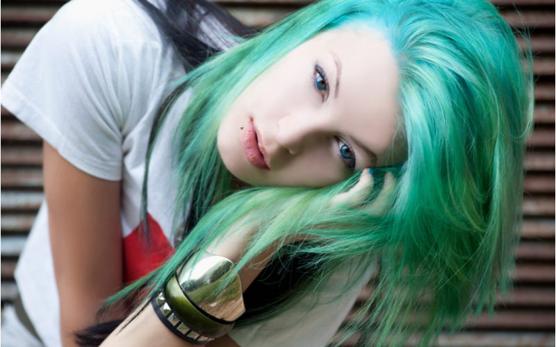 Meisje in een wit overhemd met helder groen balayage haar dat metalen armbanden draagt die haar gezicht vasthouden