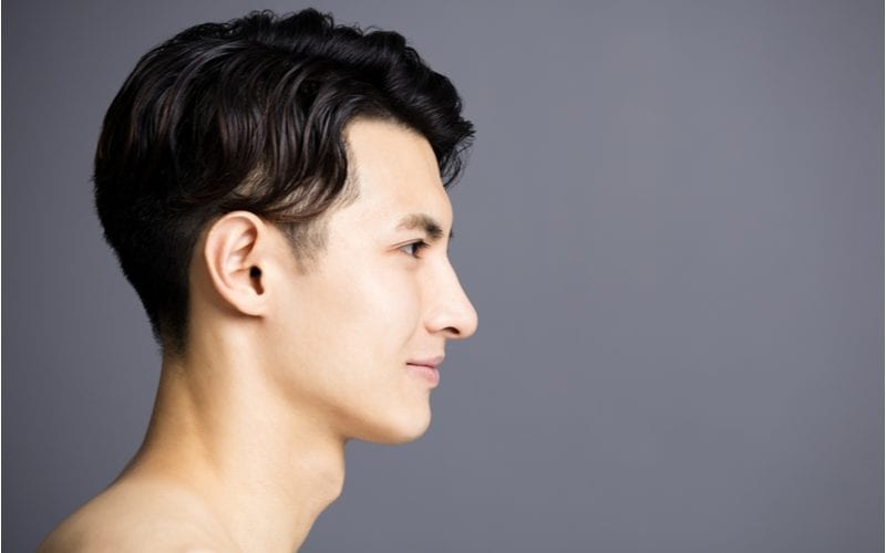 Zijprofiel van een Aziatische man die recht vooruit kijkt in een studio op een grijze achtergrond