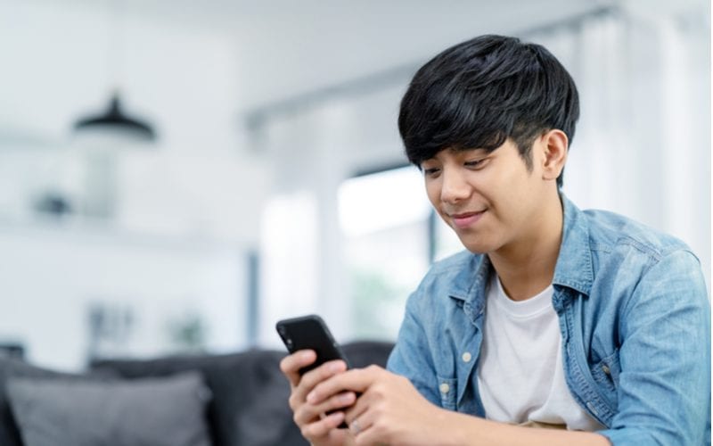 Gelukkige aziatische tiener die naar een telefoon kijkt en een onder de jongeren populair aziatisch mannenkapsel draagt