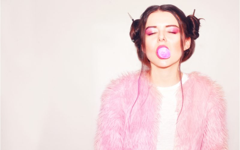 Meisje met gekke space buns in een roze boa knalt haar roze kauwgom op met roze lippen