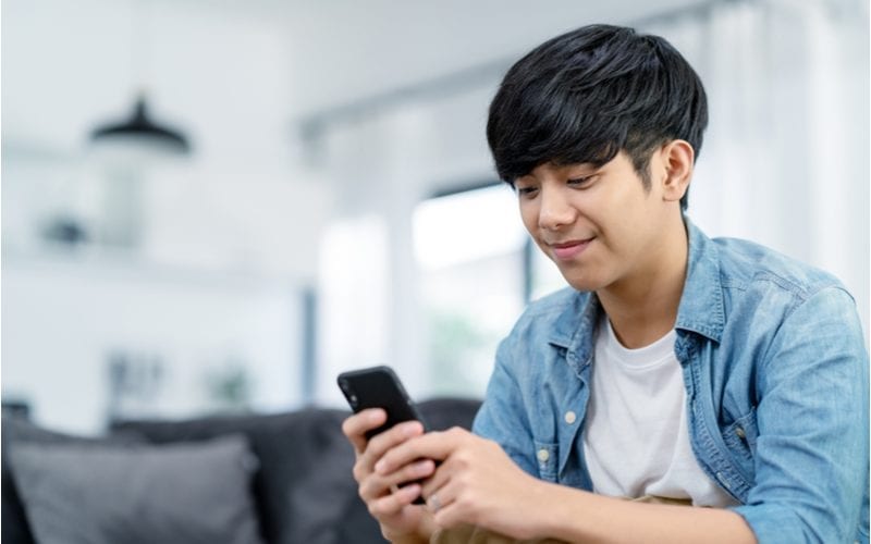 jonge aziatische man zit binnen en kijkt naar zijn telefoon