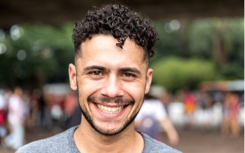 Braziliaanse man met een strak gekrulde kom en een dunne baard en snor staat buiten te glimlachen