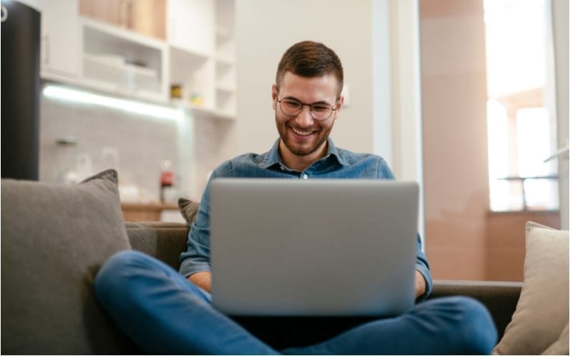 Man op zijn laptop met zijn benen gekruist draagt een bril en lacht