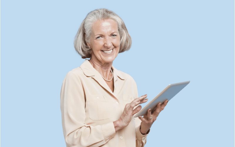 Oudere vrouw met een Blunt Cut Bob die een ipad vasthoudt en glimlacht in een blauwe kamer