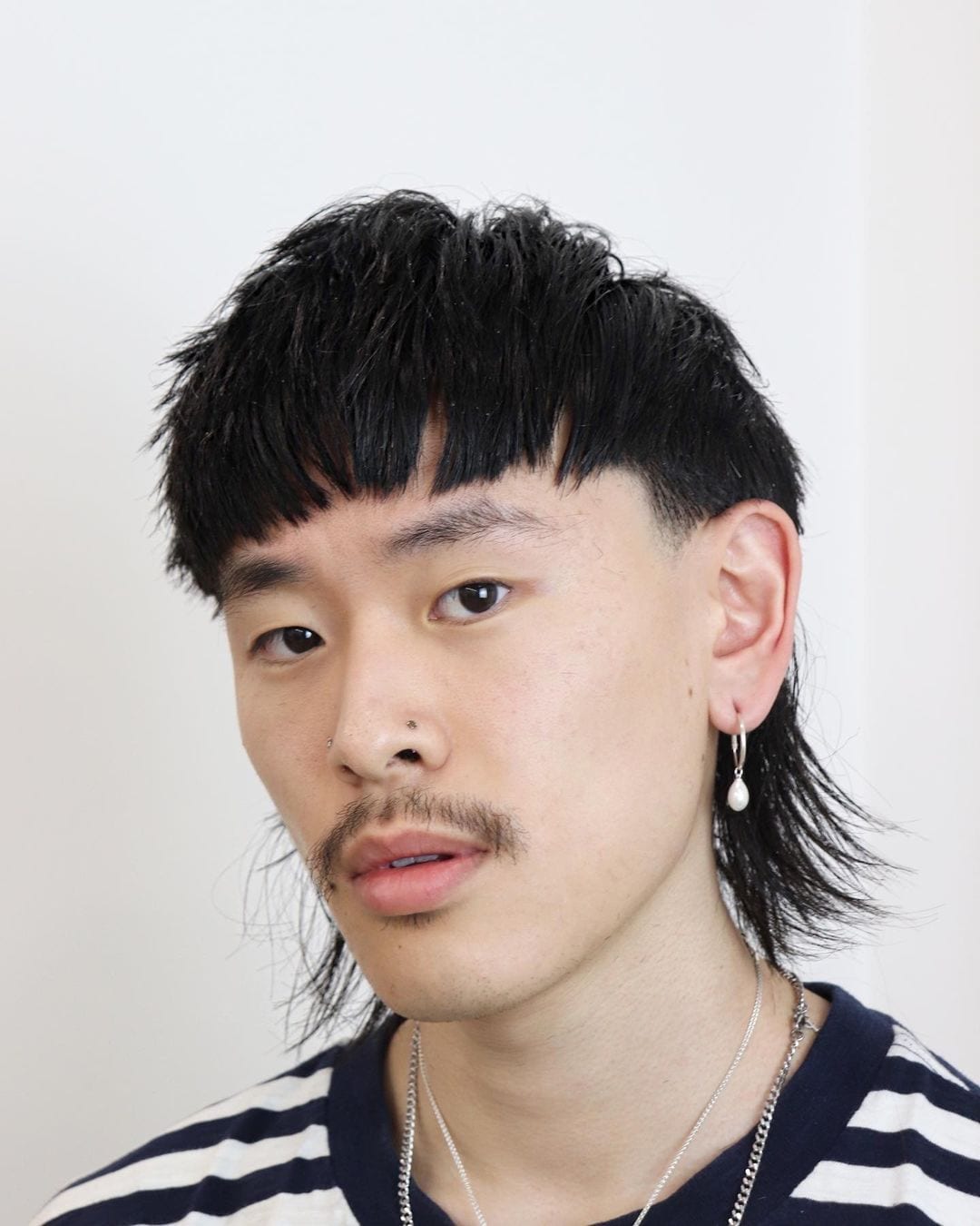 Aziatische man met een komvormige mullet en een smerig uitziende vieze snor en langere oorbellen