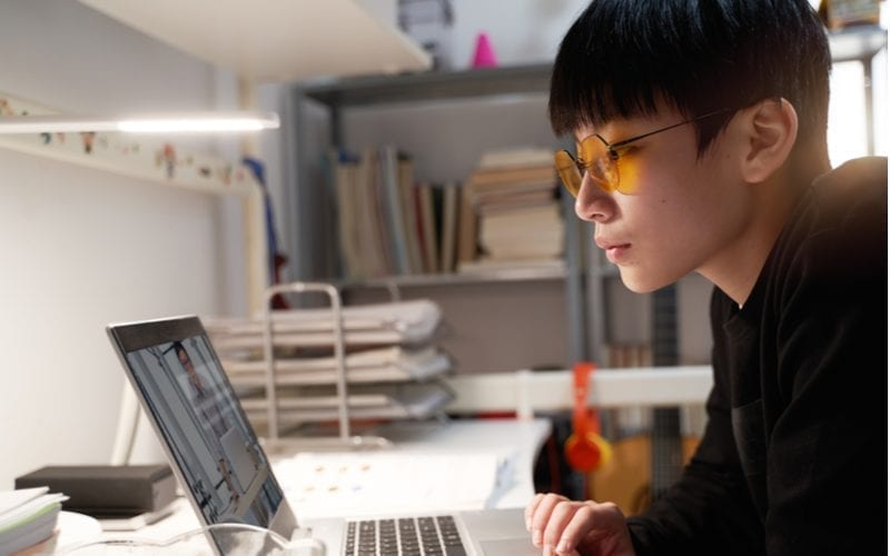 Jonge Aziatische jongen die naar een laptop kijkt en een kapsel met twee blokken draagt