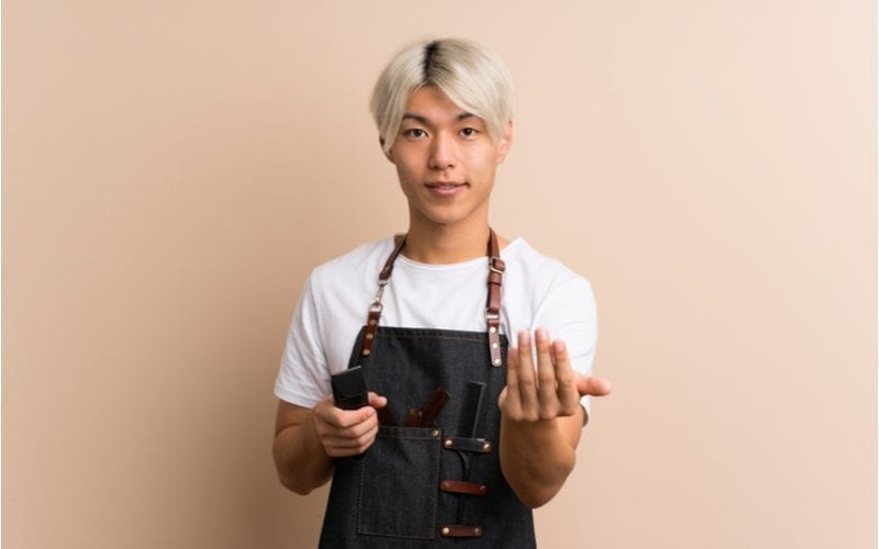 De jonge Aziatische man met blond geverfd haar houdt elektronisch scheerapparaat en moties vast 