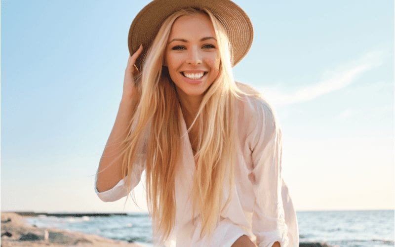 Fijn haar met lange lagen op een vrouw op een strand met een bruine rieten hoed