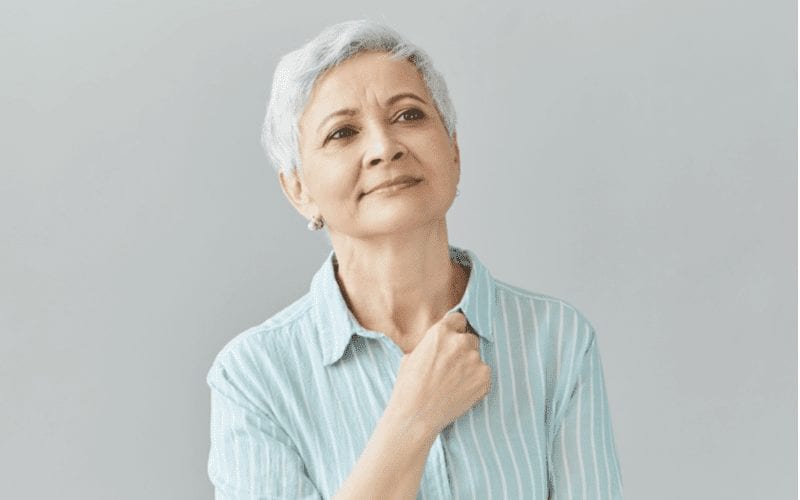 Peinzende vrouw van boven de 60 met een kort kapsel die haar rechtervuist tegen haar borst houdt