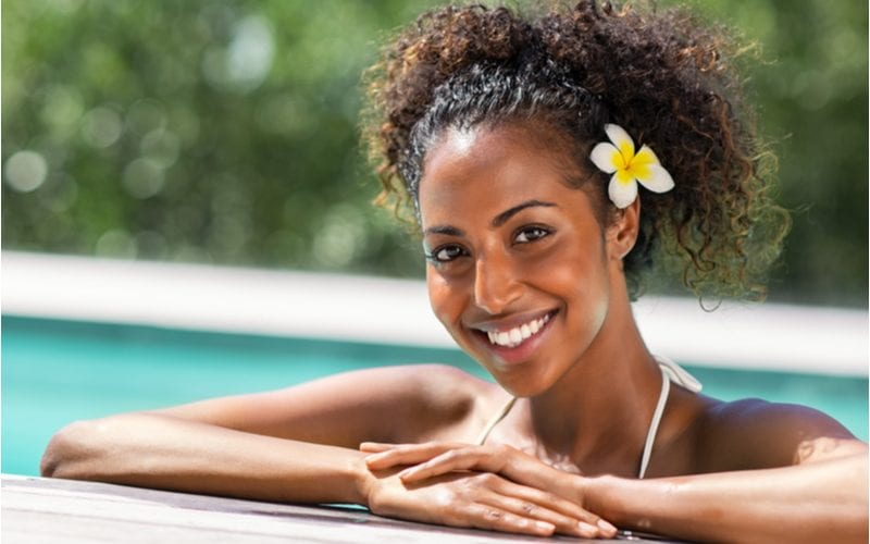 Vrouw met natuurlijk kapsel (twin puffs) en een bloem in haar haar die bij het zwembad ontspant