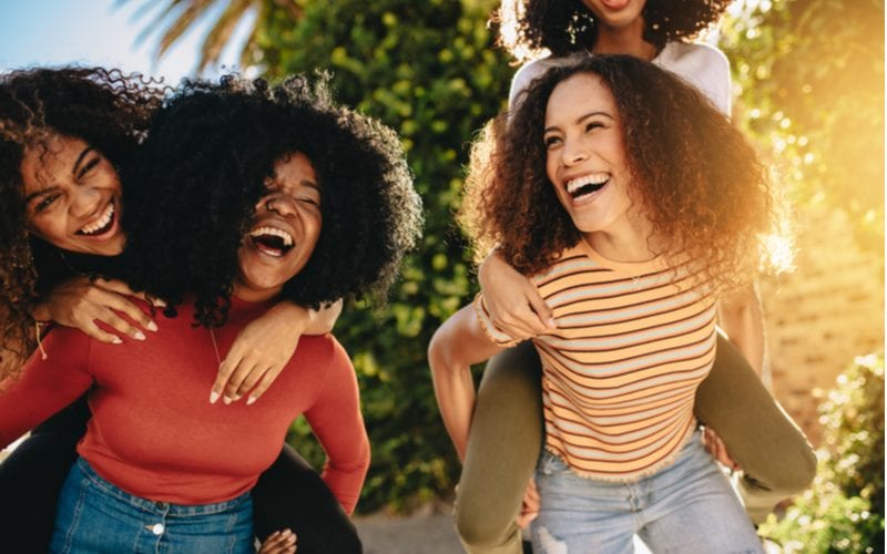 Afro-Amerikaanse vrouwen met natuurlijk haar geven elkaar ruggespraak en lachen buiten.