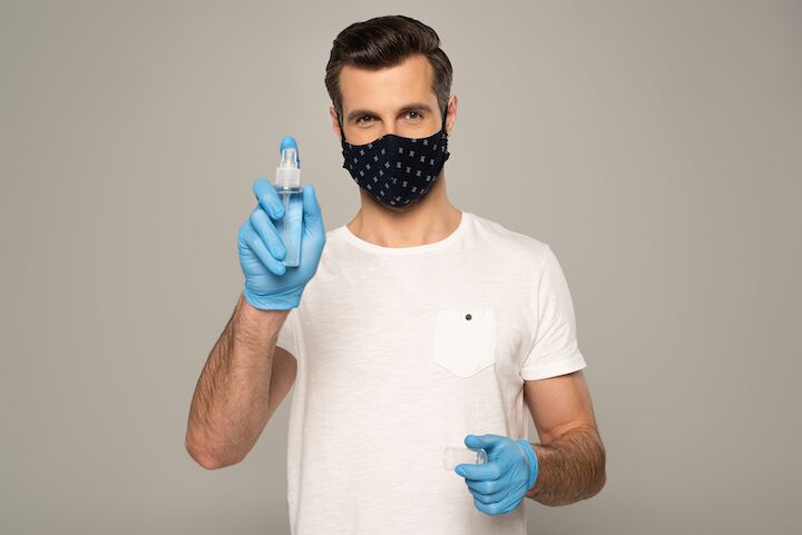Man met een masker en handschoenen die een ontsmettingsmiddel vasthouden