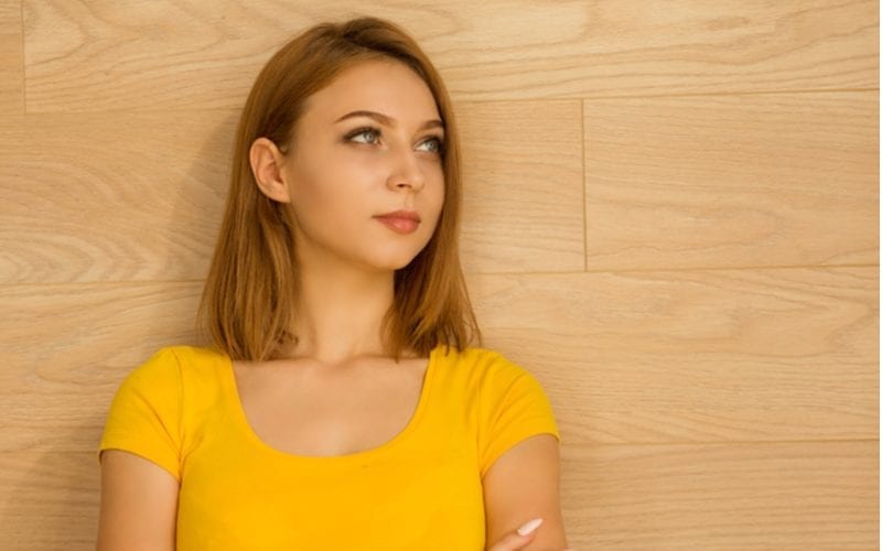 Jonge vrouw in een geel topje kruist haar armen en kijkt omhoog en naar rechts