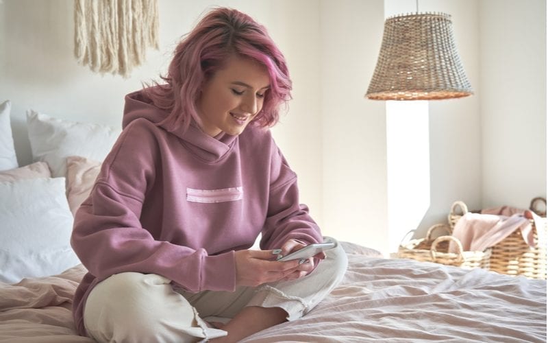 Hipster tiener kijkt naar de telefoon en kruist haar benen terwijl ze op haar bed zit