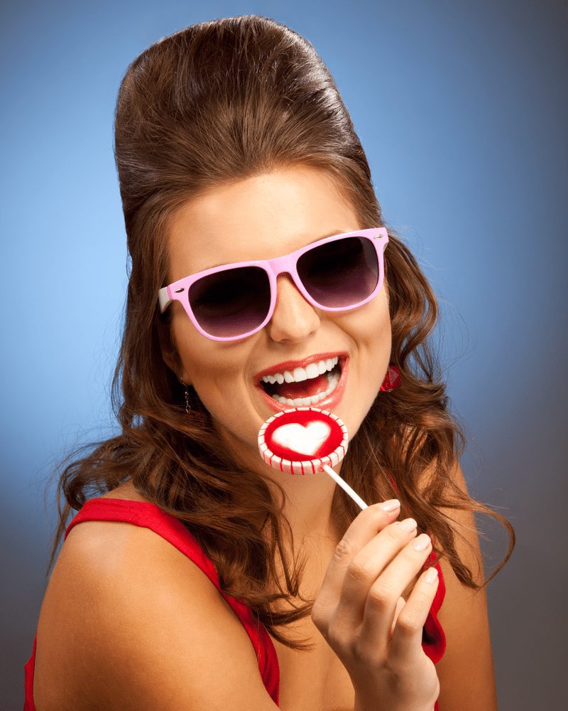 Lachende vrouw met een lolly lacht en draagt een roze zonnebril met een slecht kapsel