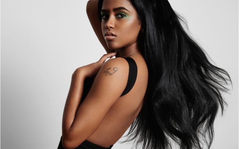Jong afrikaans amerikaans model met een lang vloeiend zwart weave kapsel houdt haar linkerarm tegen haar nek