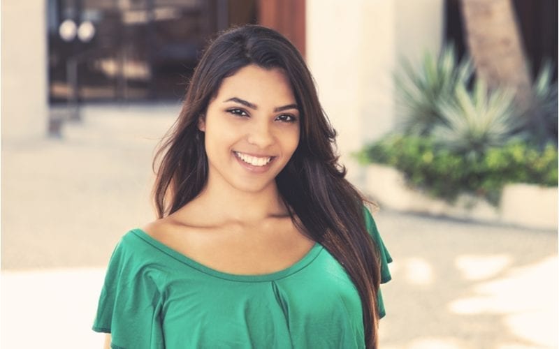 Jonge vrouw in een groene blouse lacht naar de camera en draagt een Latina kapsel dat prachtig is