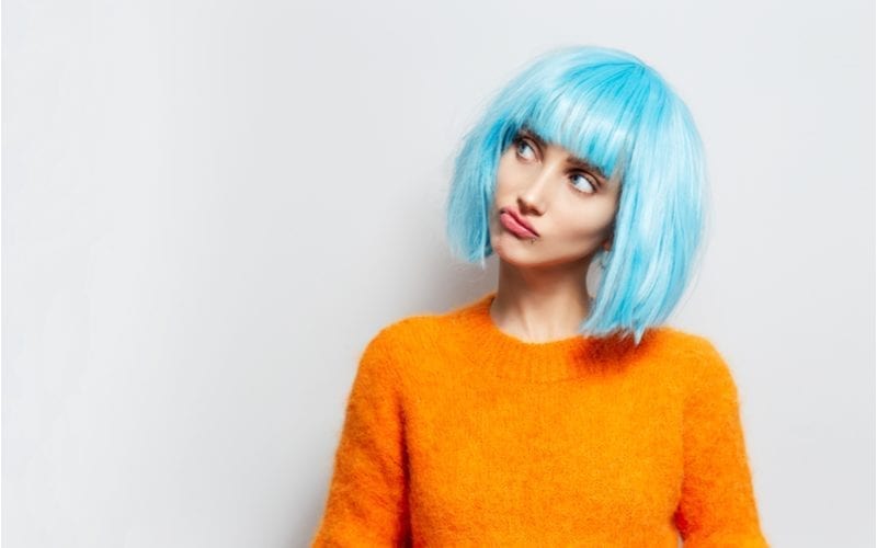 Persoon in een blauw e-girl kapsel pruik kijkt rechts omhoog met een oranje trui