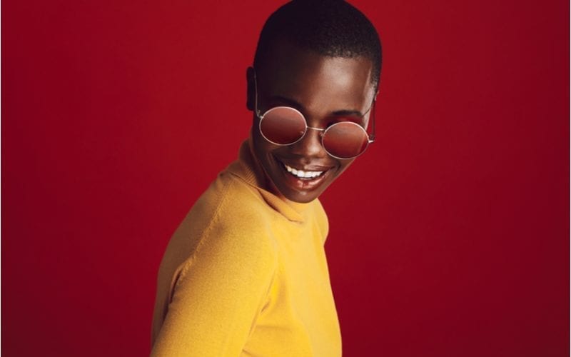 Mooi jong afrikaans amerikaans model met ronde zonnebril staand tegen rode achtergrond