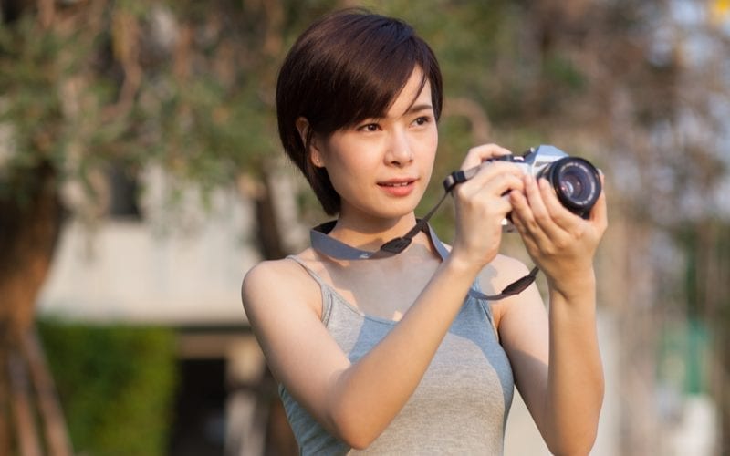 Kort harige vrouw is aziatisch en draagt haar camera om haar nek