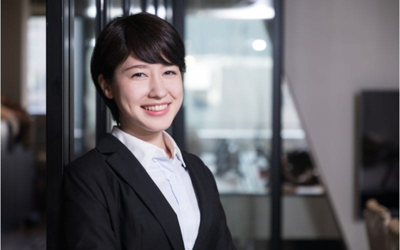 Aziatische vrouw met kort haar lacht en draagt een zwart pak met een wit shirt