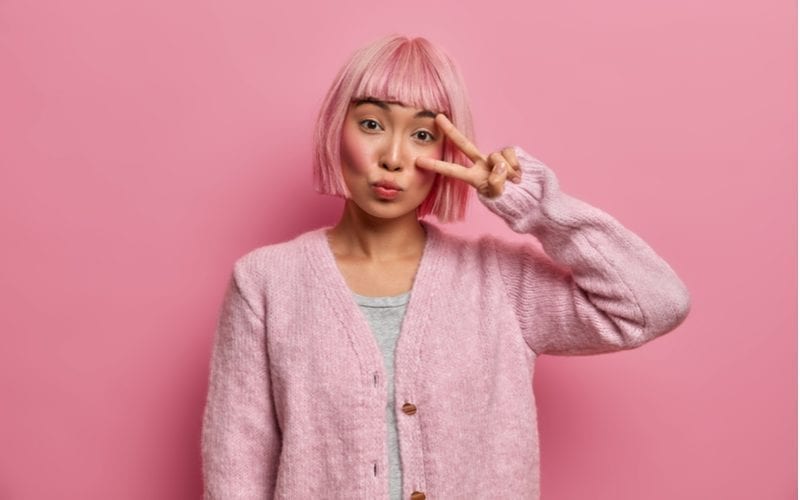 Aziatische kort haar vrouw met roze haar staat voor een roze muur
