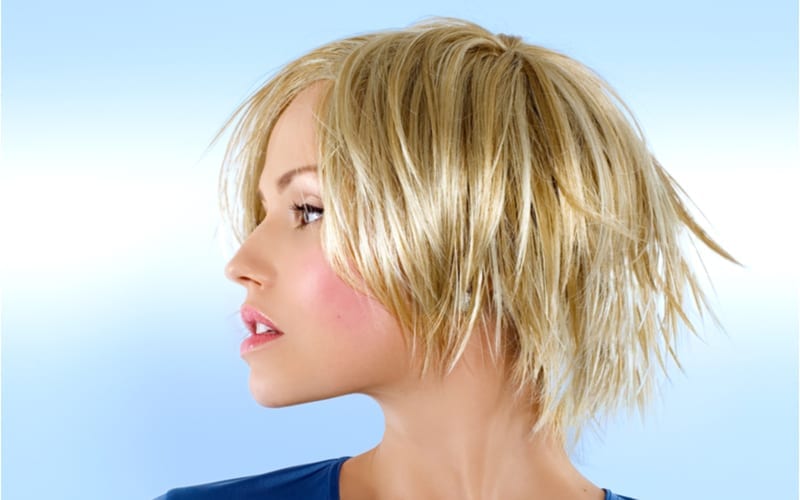 Blond model in studio met kort kapsel en blauw shirt tegen een lichtblauwe achtergrond.