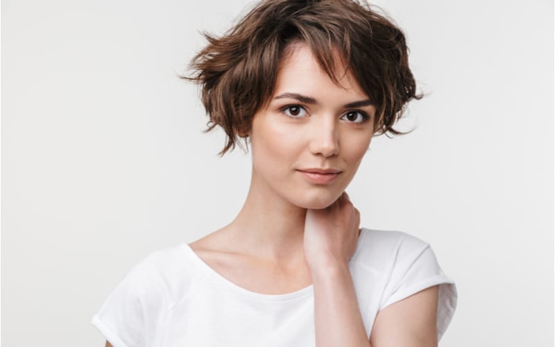 Portret van jonge vrouw met kort bruin haar in basis t-shirt kijkend naar camera terwijl ze staat geïsoleerd over witte achtergrond