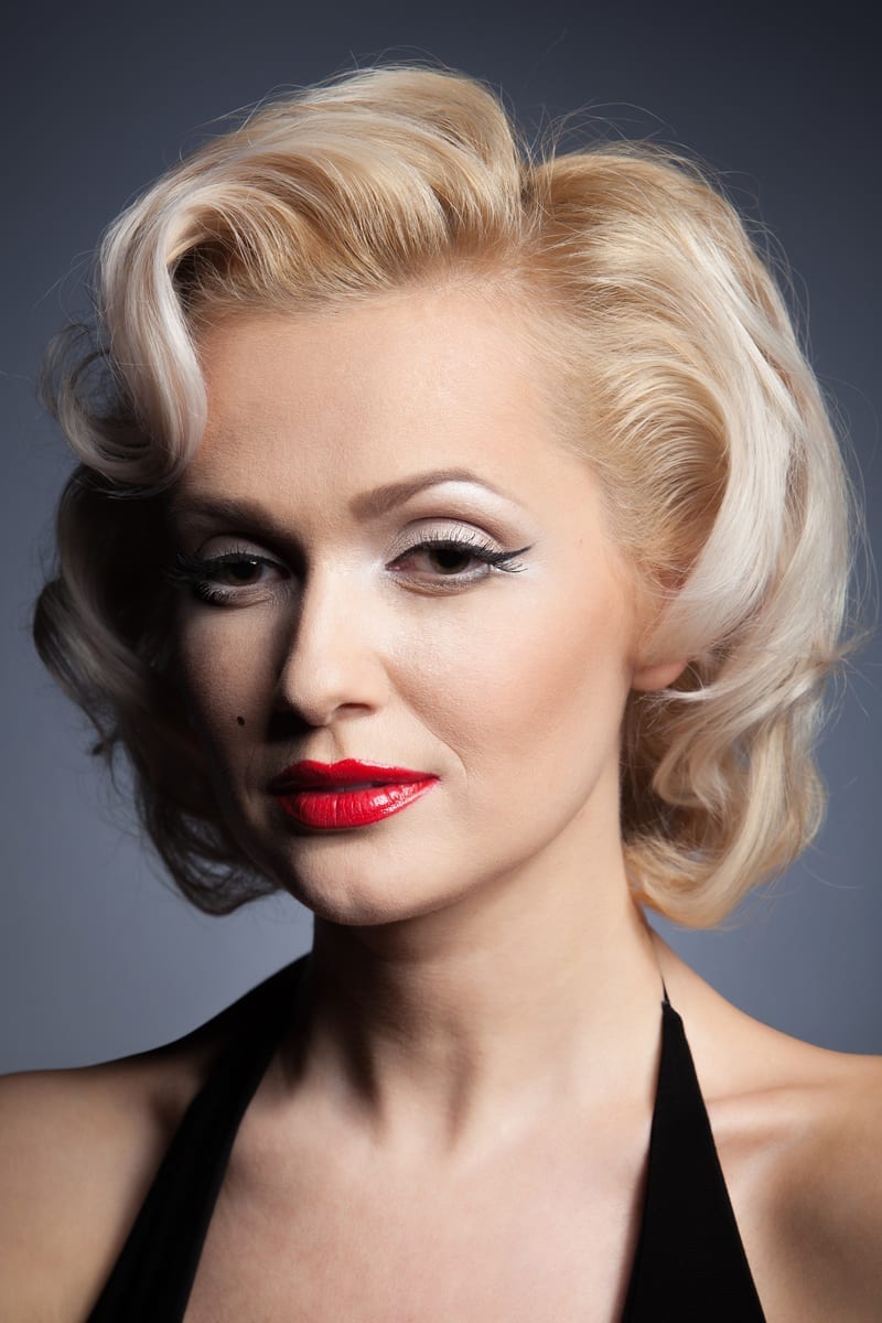 Mooi blond meisjesmodel zoals Marilyn Monroe in zwarte kleding met rode lippen op grijze achtergrond