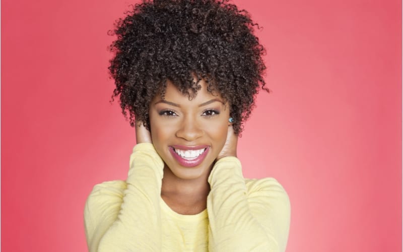 Portret van een vrolijke Afro-Amerikaanse vrouw met een kort kapsel met de handen over de oren