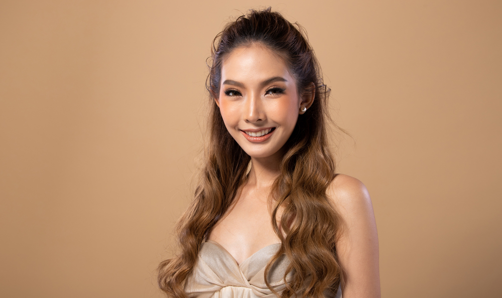 Schattige dunne Aziatische vrouw met lichtbruin haar in een zilveren jurk die glimlacht