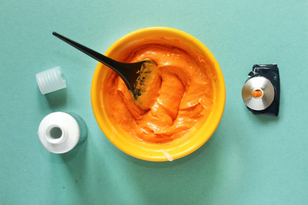 Plat beeld met oranje kleurstof in een gele kom voor een stuk over does permanent hair dye fade