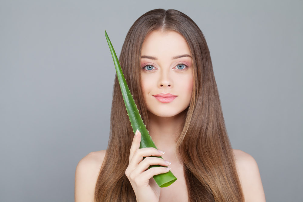 Vrouw houdt een aloë plant tegen haar gezicht vraagt zich af hoe vaak kan ik aloë vera gel op mijn haar gebruiken