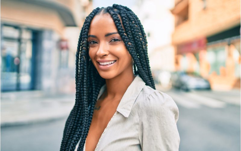 Vrouw met doos vlechten in business casual kleding staande bij een straat kruising