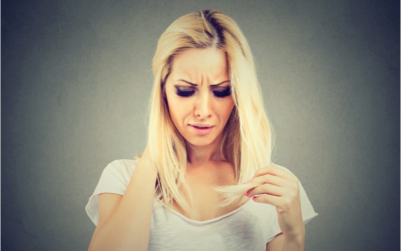 Vrouw kijkt naar haar haar en vraagt zich af hoe overkleurd haar te herstellen.