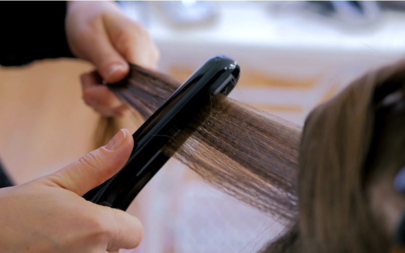 Voor een stuk over het beste product om zwart haar steil te maken, foto van een stylist die een stijltang gebruikt op donkerbruin haar