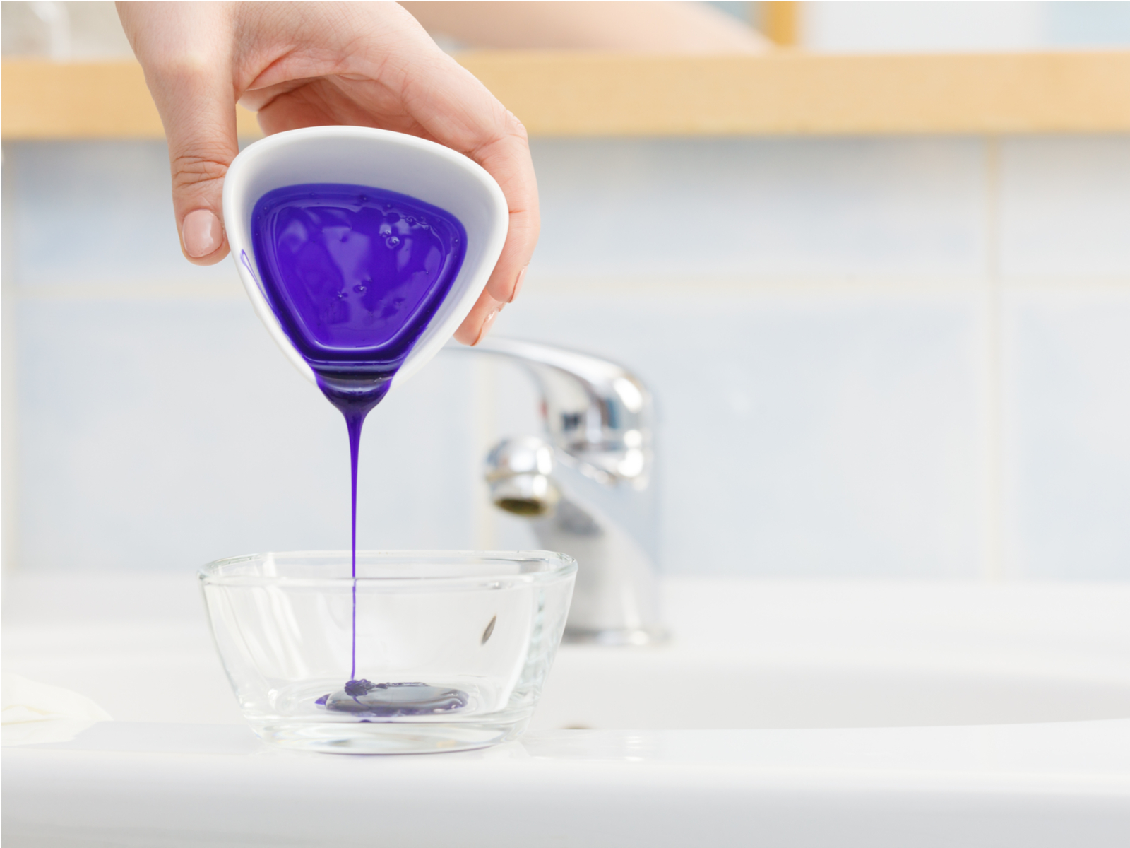 Vrouw giet paarse shampoo in een glazen kom voor een stuk getiteld breng je toner aan op nat of droog haar