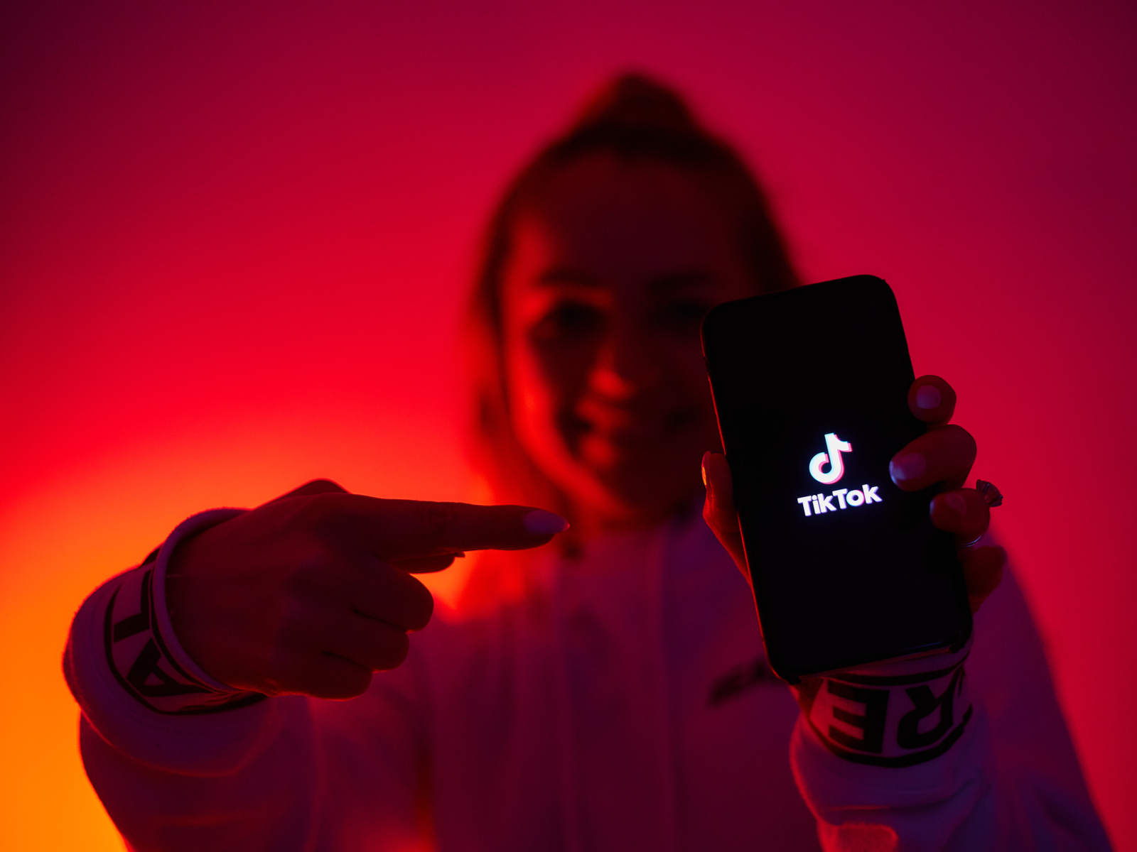 Jonge vrouw wijst naar een telefoon met de TikTok app voor een stuk over TikTok haartrends