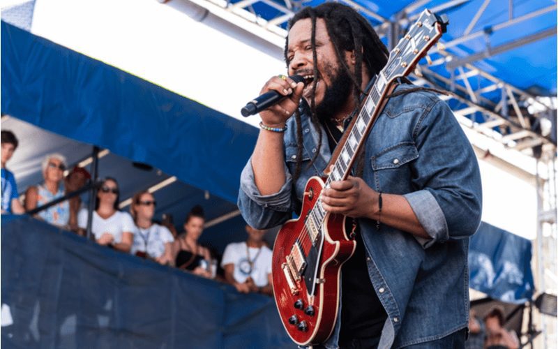 Beeld van Steven Marley die in een microfoon zingt en een gitaar vasthoudt terwijl hij met freeform dreads rockt.