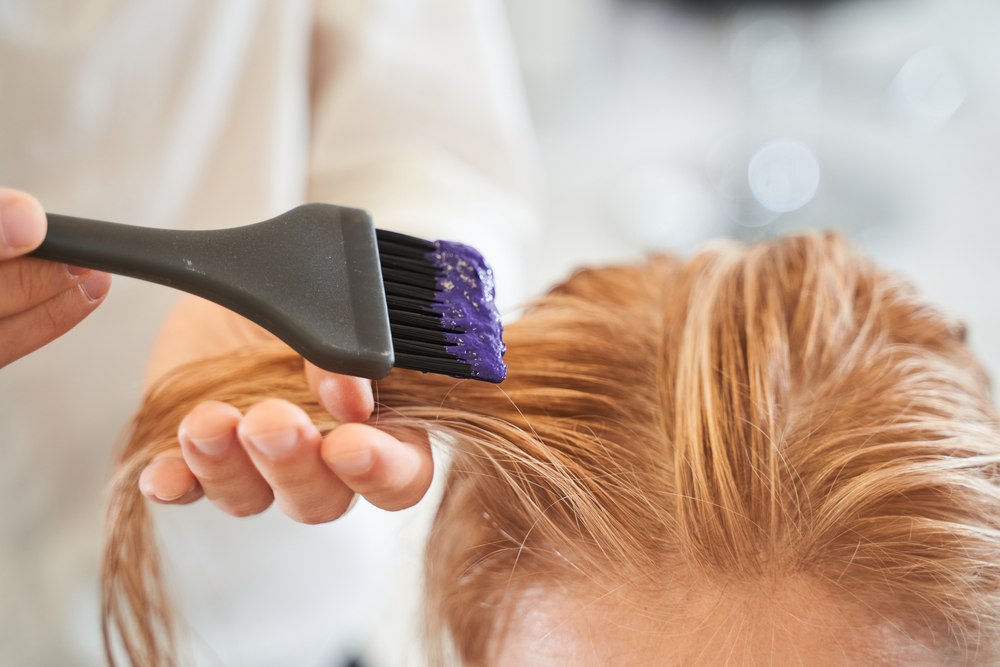 For a piece on hair highlights vs hair streaks, a woman getting a hand-painted dye applied to her blonde hair