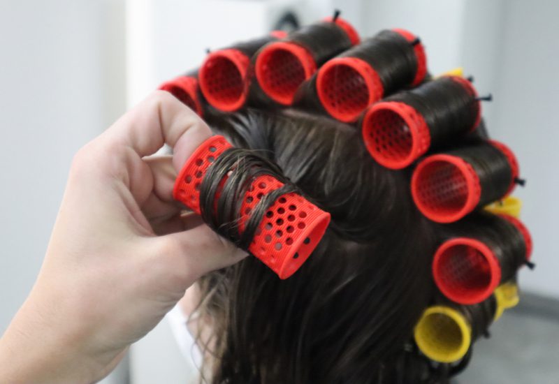 Voor een stukje over warmteloze krullen, een vrouw met een bos plastic warmteloze krulspelden in haar haar met een hand die een van hen aan de linkerkant aanraakt