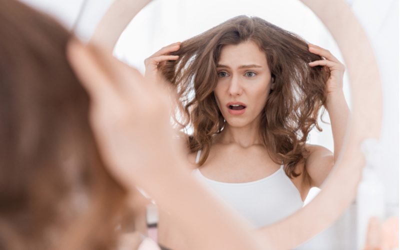 Voor een stuk over hoe van vet haar af te komen, houdt een vrouw haar haar uit en kijkt in een spiegel met een geschokte uitdrukking op haar gezicht.