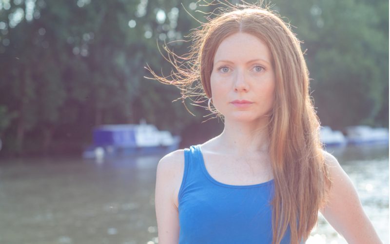 Vrouw met statisch haar staat in een blauw shirt buiten naast een meer