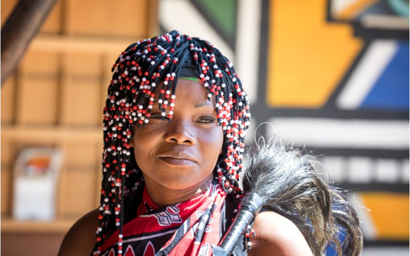 Vrouw laat zien hoe je kralen in het haar doet in traditionele Afrikaanse kleding