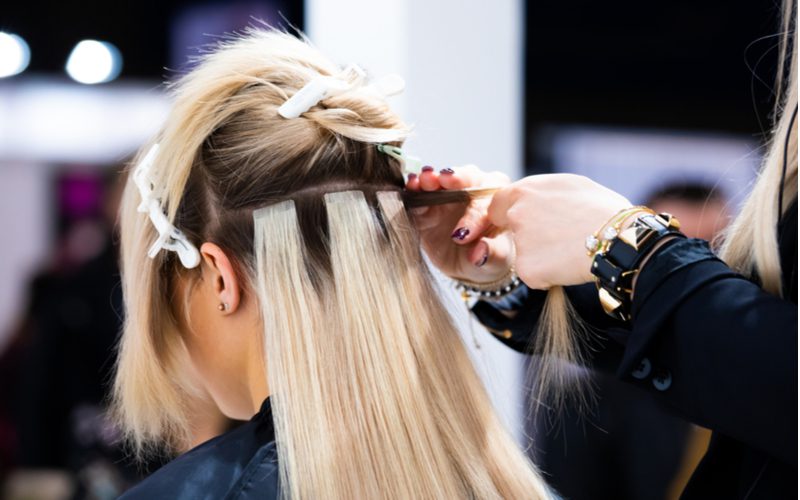 Om te symboliseren hoe lang haarextensies meegaan, laat een vrouw haar haar knippen en doen door een vrouw in een kapsalon