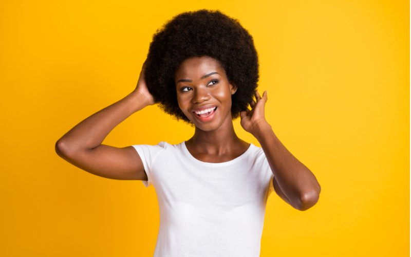 Voor een stuk over hoe je een afro maakt, staat een vrouw en houdt de achterkant van haar hoofd vast terwijl ze een wit shirt draagt