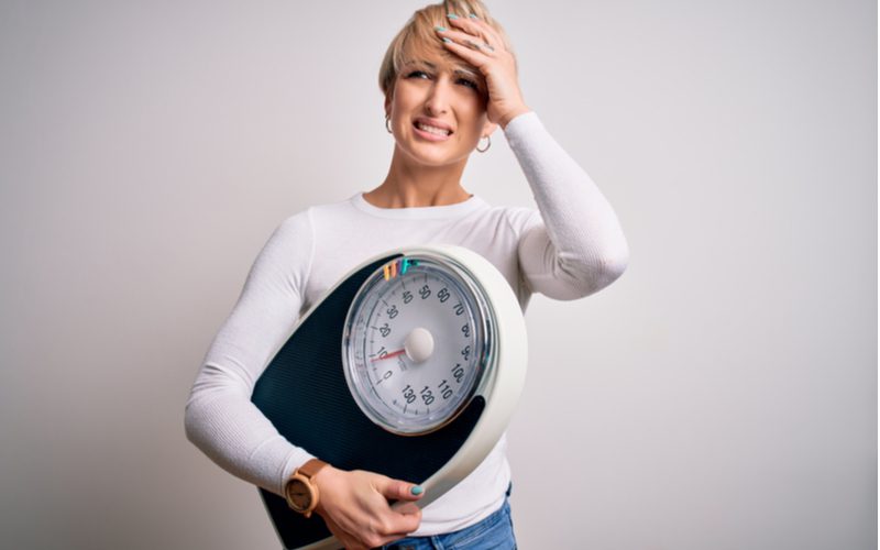 Vrouw met een weegschaal in de ene hand en haar haar in de andere voor een stuk over hoeveel weegt haar