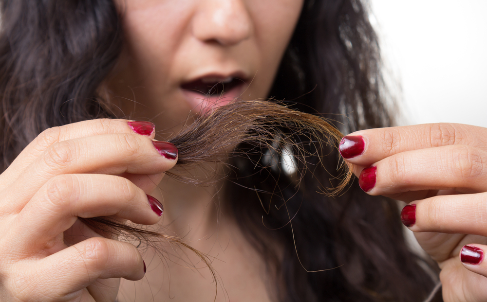 Vrouw kijkt naar haar haar in ongeloof dat ze gespleten haarpunten heeft